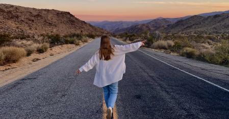 Una ragazza alla pari corre a braccia aperte lungo l'autostrada nel deserto