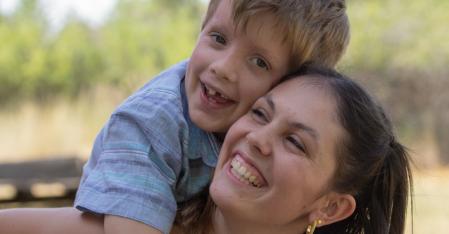 Au pair che porta il bambino della famiglia ospitante sulla schiena, entrambi sorridenti alla telecamera